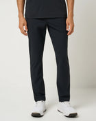 Person wearing black TravisMathew pants and white shoes on a light gray background