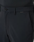 Close-up of dark charcoal gray performance trousers showing the waistband, button closure, belt loops, front pocket, and a small black TravisMathew label.